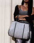 Person holding the Anya & Niki gray neoprene tote bag with shiny silver adjustable sides and cord handles. 