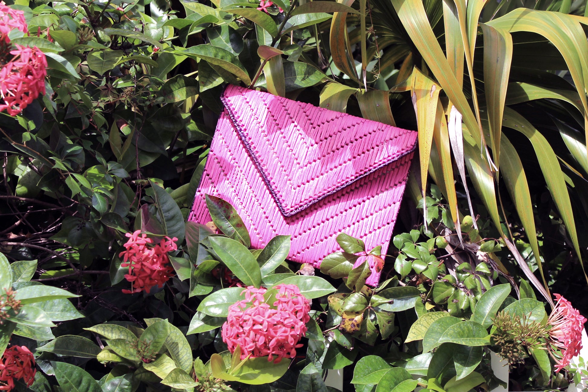 Bright pink woven raffia straw clutch nestled into flowers and foliage. 