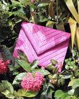 Bright pink woven raffia straw clutch nestled into flowers and foliage. 