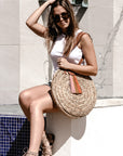 person holding natural seagrass round straw bag with leather handles and suede tassel closure.