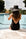 Person sitting on edge of pool wearing the Anya & Niki Big Hat in black straw.