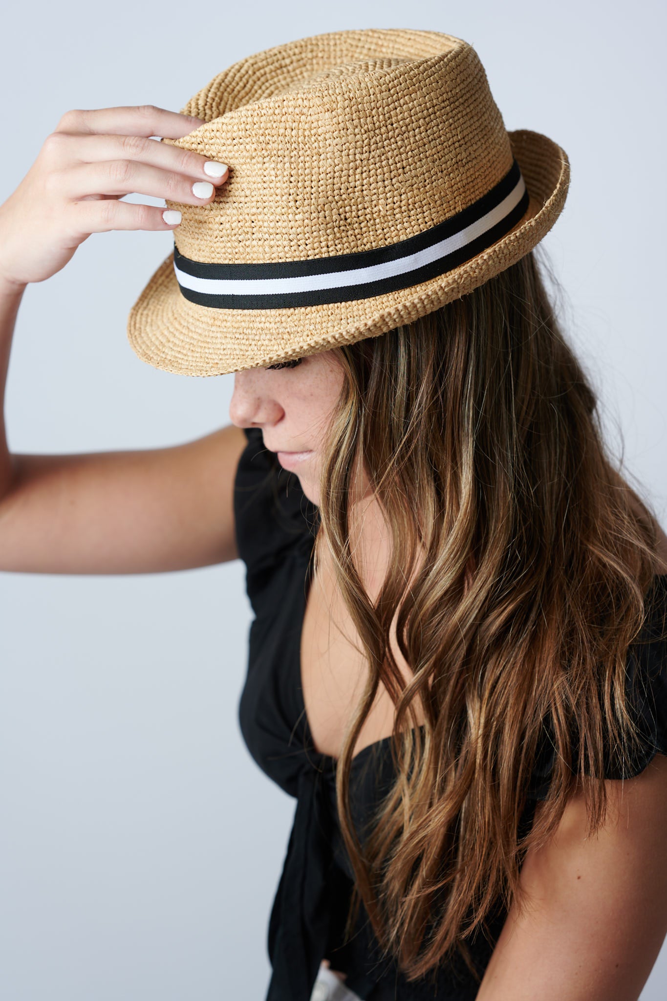 Person wearing natural colored crochet straw fedora hat with black &amp; white stripe band.