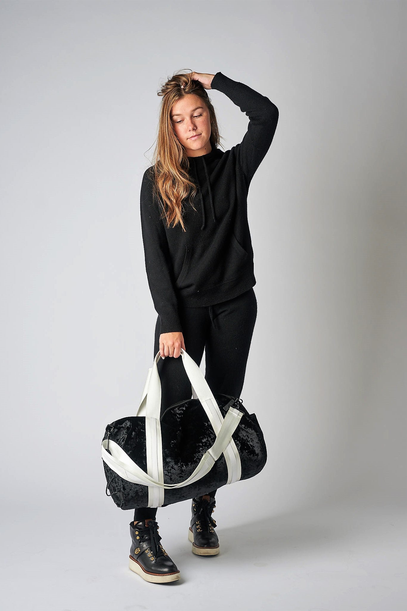 person holding black velour duffel bag with white straps and leather details