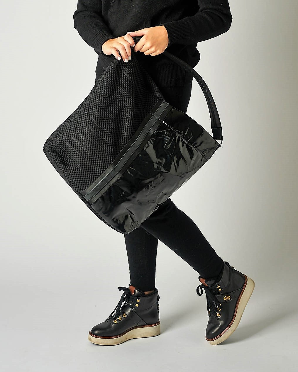 person with black mesh and glossy vinyl sporty tote bag with black leather and webbing details.