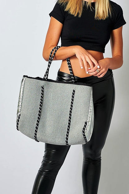 Person holding the Anya & Niki gray neoprene tote bag with shiny silver adjustable sides and cord handles. 
