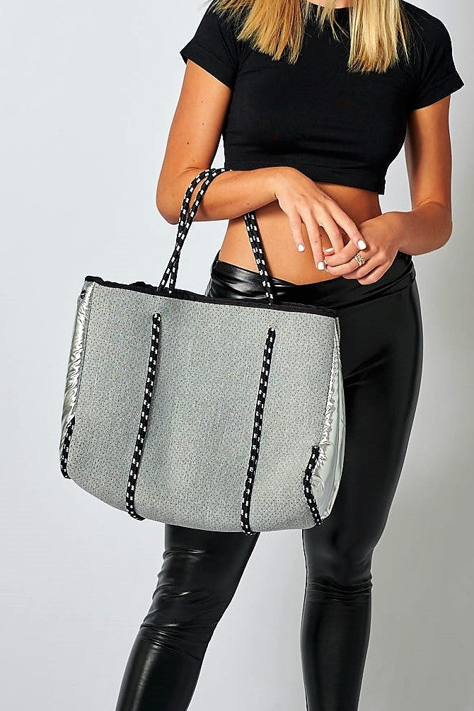 Person holding the Anya &amp; Niki gray neoprene tote bag with shiny silver adjustable sides and cord handles. 