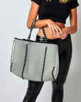 Person holding the Anya & Niki gray neoprene tote bag with shiny silver adjustable sides and cord handles. 