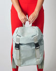 Person holding gray high gloss backpack with gray leather and webbing details.