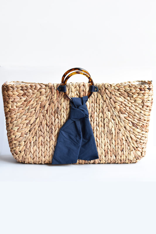 Extra-large hyacinth straw tote with faux torte circle handle and navy tie front.