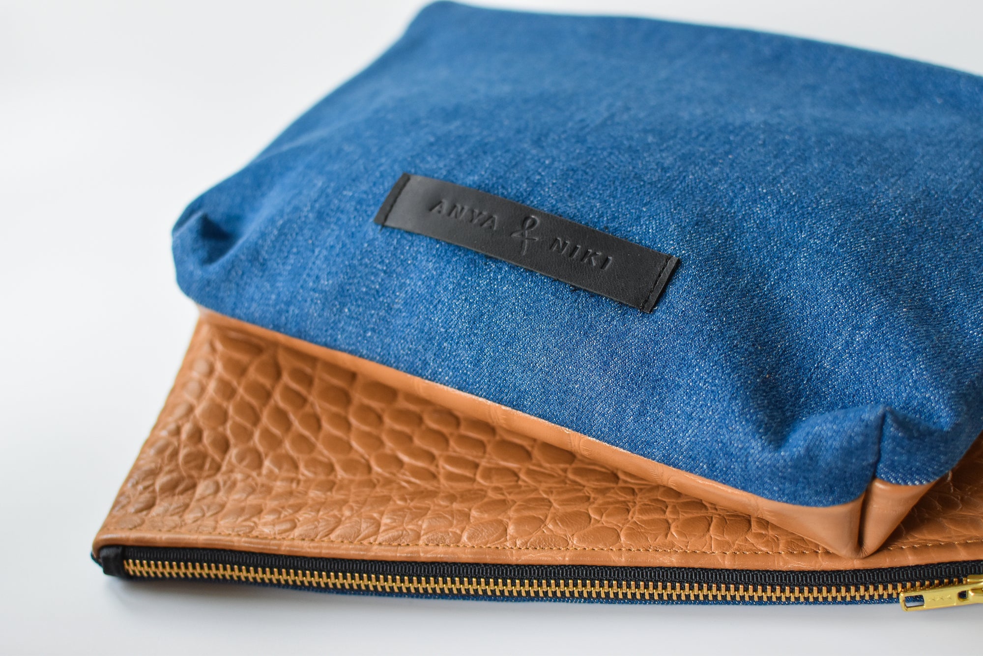 Medium wash denim and caramel colored embossed leather skin medium pouch with brass zipper and leather logo label.