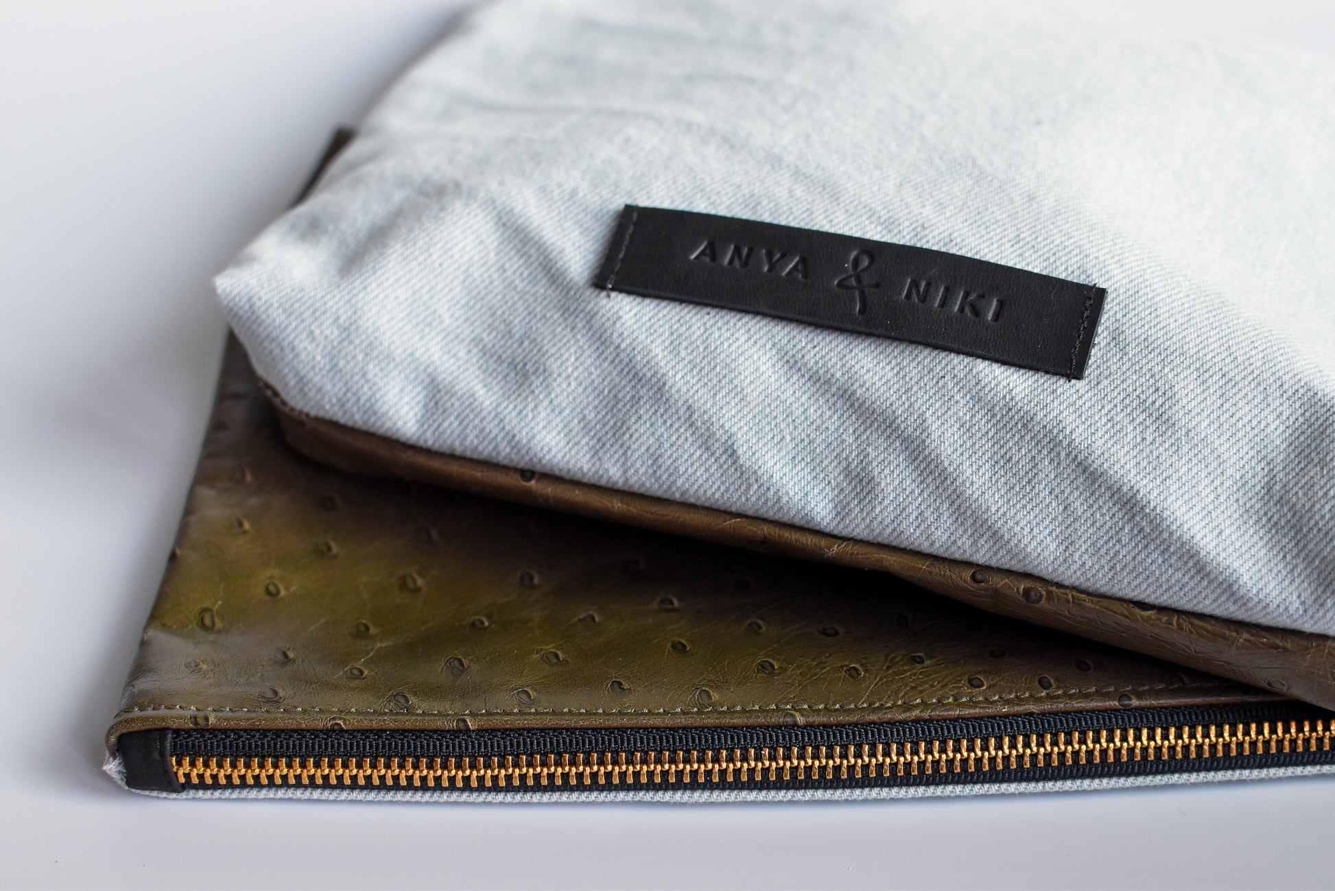 Bleached denim and fern colored embossed leather skin medium pouch with brass zipper and leather logo label.